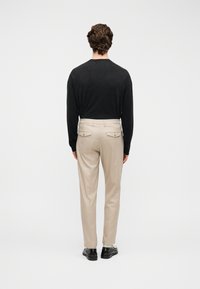 Chemise noire à manches longues, pantalon beige avec poches arrière, et chaussures noires. Design simple avec une coupe décontractée et un tissu léger.