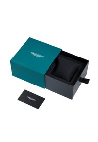 Teal box med en silverlogga, som innehåller en svart kudde. Inkluderar ett platt svart kort med en silverlogga. Lådan har en dragflik för att öppnas.