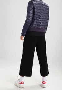 Mörkblå puffjacka med kviltad textur och ribbad nederkant, tillsammans med lösa svarta cropped byxor och vita sneakers med röda detaljer.