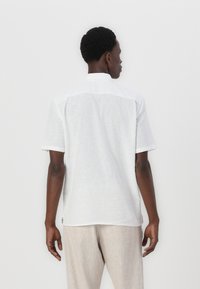 Camicia a maniche corte bianca realizzata in tessuto leggero. Presenta un colletto a camicia e una superficie liscia. La vista posteriore mostra un fit rilassato.