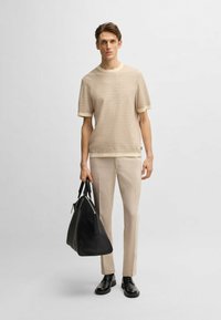 Maglioncino corto beige con texture e maniche corte, dotato di colletto e polsini crema a contrasto, abbinato a pantaloni beige chiaro e una borsa a tracolla nera.