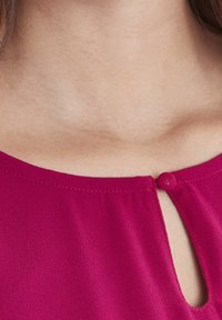 Blusa fucsia con scollatura tonda, dettaglio a chiave e piccolo bottone sul retro. Tessuto liscio e leggero.
