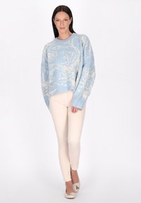 Pulover tricotat de culoare albastru deschis, cu un model abstract crem, croială lejeră, decolteu rotund, mâneci lungi, asortat cu pantaloni skinny bej și încălțăminte bej.