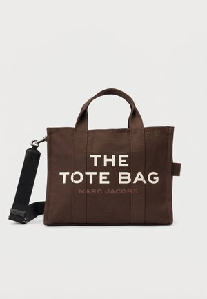 Sac fourre-tout en toile marron avec poignées courtes, bandoulière noire détachable et "THE TOTE BAG MARC JACOBS" imprimé à l'avant.