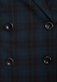 Dvojřadový blazer vyrobený z tmavě kostkované tkaniny v námořnické, zelené a hnědé barvě, s kulatými černými knoflíky a hladkou texturou.