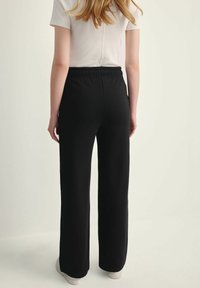 Czarne spodnie z szerokimi nogawkami i elastycznym paskiem, wykonane z miękkiego materiału. Projekt charakteryzuje się luźnym fasonem, bez widocznych wzorów czy zdobień.