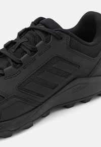 Czarne sportowe buty z teksturowanym materiałem siateczkowym, syntetycznymi wstawkami i gumową podeszwą z wyraźnymi wypustkami zapewniającymi dobrą przyczepność.