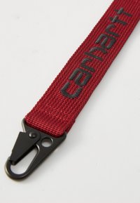 Correa trenzada roja con el logo negro de "Carhartt"; cuenta con un accesorio de clip negro para sujeción, textura resistente y diseño plano.