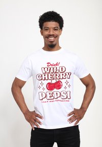 Bílá tričko s červenou a černou grafikou s třešněmi a textem "Pij! DIVOKÁ TŘEŠNĚ PEPSI LEHKÉ A OSVĚŽUJÍCÍ". Krátké rukávy.