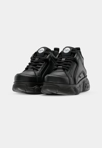 Ett par svarta Buffalo plattformssneakers med tjocka texturerade sulor och logotyper på tungan och sidan, visade på vit bakgrund.