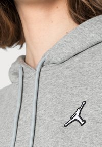 Sudadera gris con cordón y un logo Jumpman bordado en blanco y negro en el pecho, fabricada con un tejido suave y de acabado texturizado.