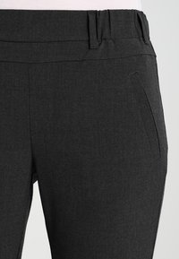 Donkergrijze broek van een gladde, gestructureerde stof. Heeft een platte tailleband, riemlussen en een zijzak op de heup.