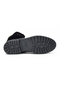 Suela de bota negra con surcos profundos para tracción, con un diseño robusto. El material parece ser de caucho con patrones texturizados y detalles de marca.