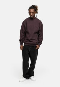 Dark purple sweatshirt with crew neck, relaxed fit, paired with loose black jeans and white sneakers. Plain fabric with no visible patterns.