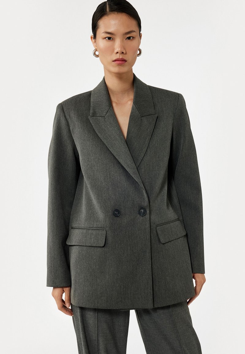 Grijze, oversized blazer met een uitgesneden kraag, dubbele knoopsluiting, twee voorzakken en een gladde stofstructuur.