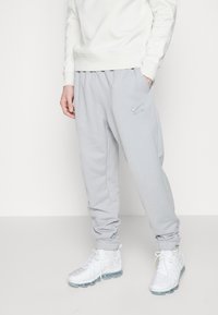 Grå sweatpants i mjukt tyg, med elastisk midja och ankelslutar, pryds av en diskret Nike-logotyp framtill. I kombination med vita sneakers.