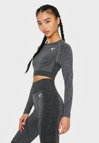 Sivi atletski crop top i tajice visokog struka imaju teksturirani materijal, duge rukave, rebraste detalje i logo akcent na topu.