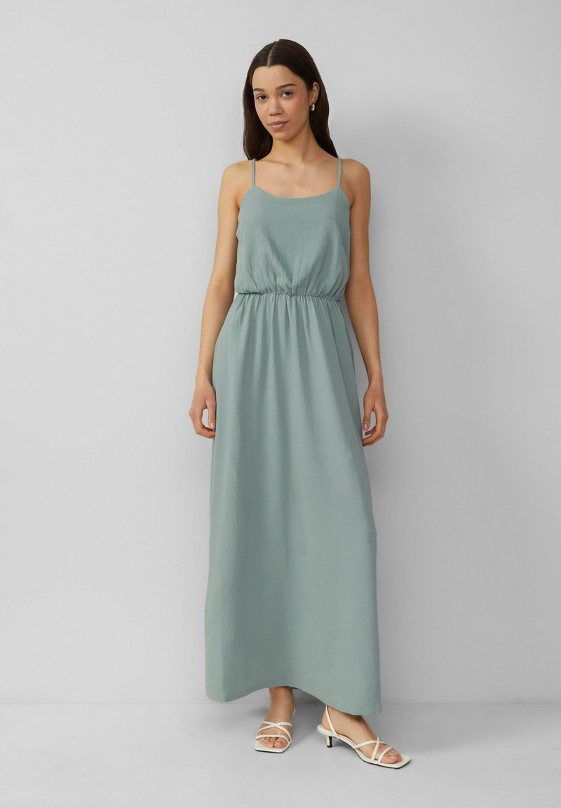 Maxi-Kleid in hellgrün, mit lockerer Passform, elastischem Bund und dünnen Trägern, kombiniert mit weißen Riemchensandalen. Glattes, strukturiertes Material.