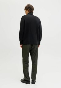 Maglione nero a maglia con colletto alto, abbinato a pantaloni verde oliva. Texture liscia, vestibilità rilassata e design semplice senza dettagli significativi.