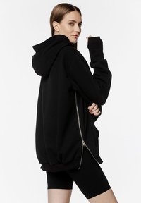 Czarny, oversize hoodie z zapięciem na zamek, długimi rękawami i kieszenią kangurką. Materiał wydaje się miękki i teksturowany, z kapturem.