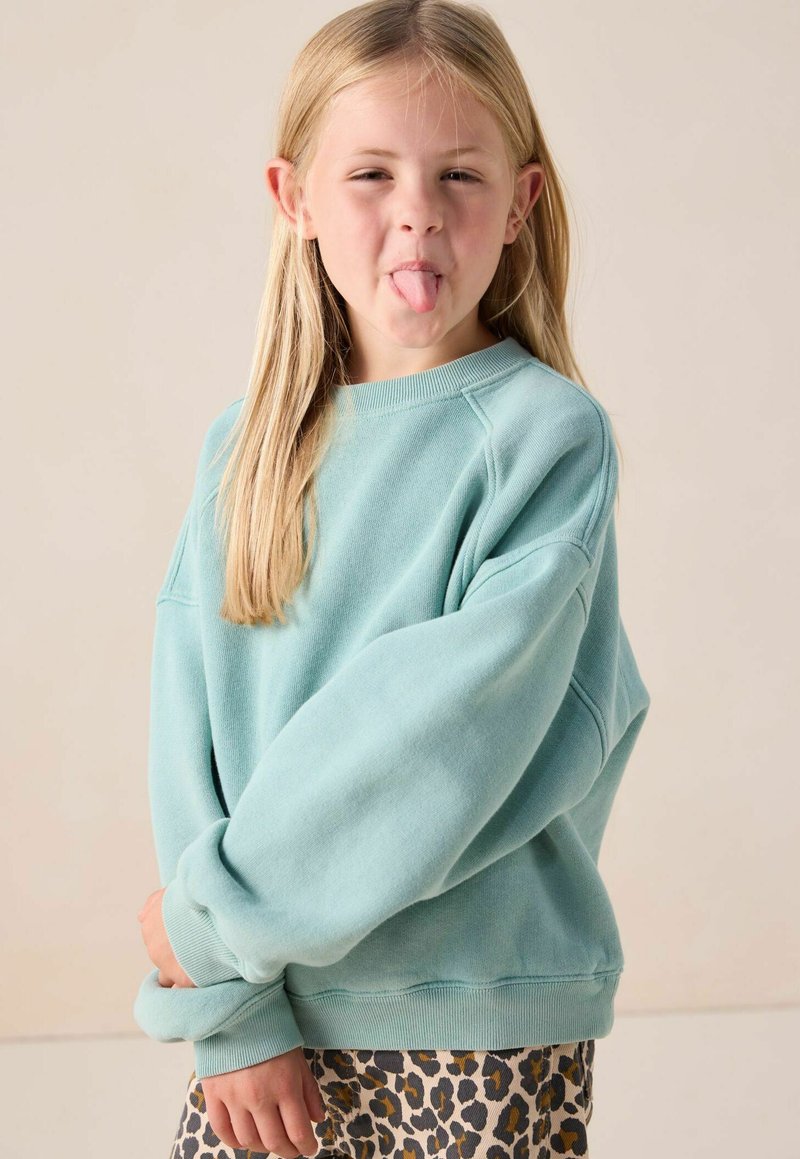 Sweatshirt vert menthe avec des manches surdimensionnées et des poignets côtelés, associé à une jupe en imprimé léopard. Texture lisse, design décontracté.