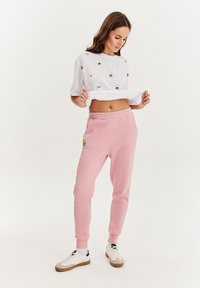 Biely skrátený tričko s viacfarebnou výšivkou zvierat, spárované s ružovými teplákmi s nášivkou loga a elastickým pásom. Neformálne tenisky.