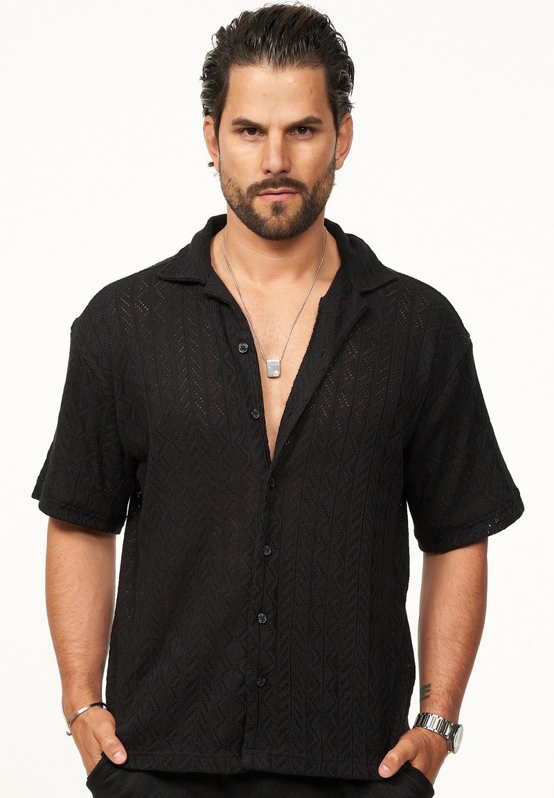 Schwarzes kurzärmliges Hemd mit Knopfleiste und strukturiertem Muster, mit offenem Kragen und mehreren Knöpfen auf der Vorderseite.