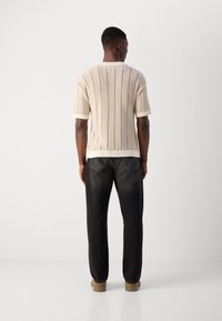 Kurzarms gestrickter Pullover in Creme mit strukturiertem Streifenmuster, getragen mit dunklen, engen Jeans und braunen Schuhen.