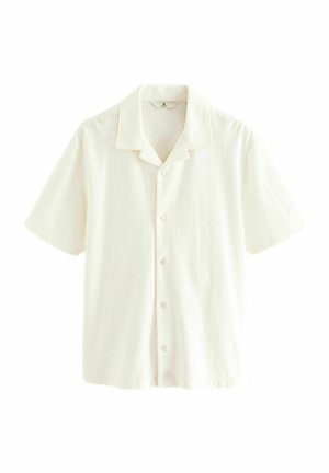 Chemise à manches courtes, de couleur blanc cassé, texturée, à boutons, avec un col style camp, posée à plat sur un fond blanc.