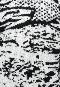 Suéter de tela de punto en blanco y negro que presenta patrones abstractos con texturas variadas, creando un contraste en toda la superficie.