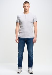 Camiseta henley gris de manga corta con tapeta de tres botones, combinada con pantalones vaqueros de denim azul y zapatillas grises. Diseño limpio y ajustado.