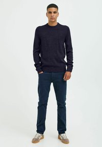 Pull en tricot navy à col rond, associé à un pantalon sombre et des baskets grises. Le pull présente des poignets et un ourlet côtelés.