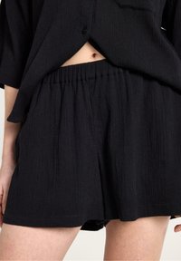 Svarta shorts i en lätt, texturerad tyg med elastisk midja. Har en lös passform och subtila veckdetaljer.