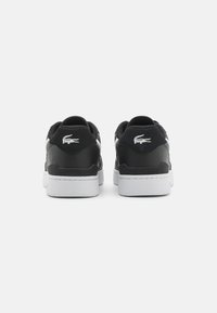 Black sneakers with white accents, featuring a textured suede heel, smooth leather sides, and a white rubber sole. Lacoste logo at heel.