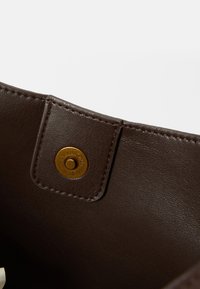 Intérieur d'un sac à main en cuir marron avec un bouton-pression doré et des coutures contrastantes, mettant en valeur une texture lisse et une couleur riche.