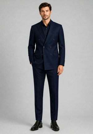 Homme debout, les mains dans les poches, portant un costume croisé bleu marine foncé, une chemise noire et des chaussures habillées noires sur un fond uni.