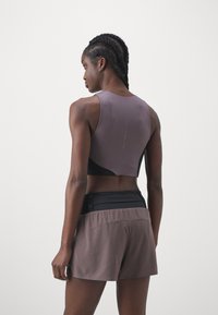 Sportoutfit mit einem lila ärmellosen Oberteil mit schwarzem Rücken und passenden braunen Shorts. Der Stoff wirkt leicht und atmungsaktiv.