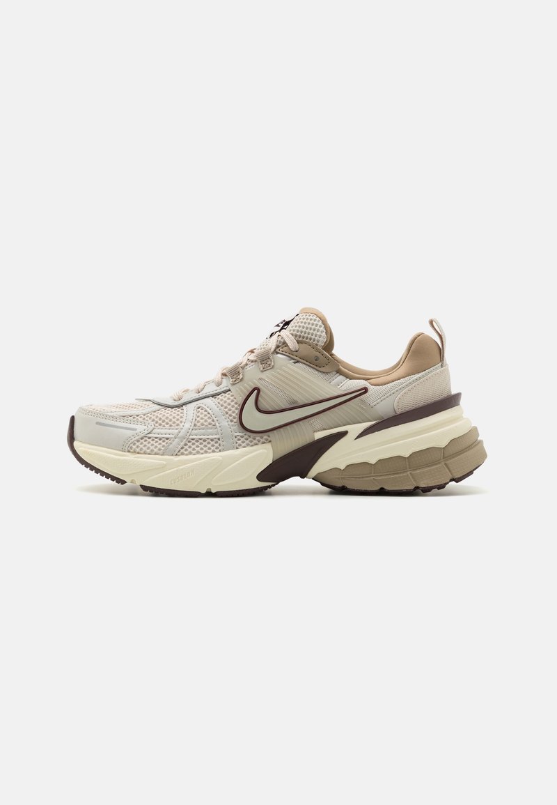 Beige en crèmekleurige sportschoenen met een gestructureerd mesh bovenwerk, een gevoerde tussenzool en een opvallende donkerbruine accent op de hiel.