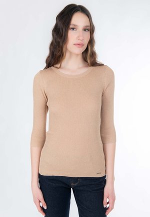 Beiger gerippter Strickpullover mit rundem Ausschnitt und Dreiviertelärmeln, kombiniert mit dunklen Denim-Jeans.