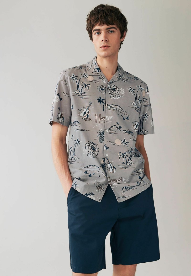 Kortärmad grå skjorta med en tropisk tryckt design som har palmer och gitarrer, i kombination med marinblå shorts, tillverkade av lättviktsmaterial.