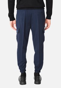 Pantaloni cargo blu navy con elastico in vita e polsini alle caviglie, dotati di tasche laterali e tasca utility con dettaglio clip. Tessuto dalla texture liscia.