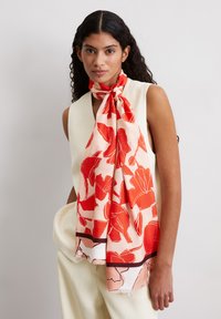 Pañuelo de seda con un patrón floral en un intenso rojo sobre un suave fondo melocotón, con un borde oscuro en contraste y una textura suave.