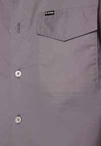 Camisa gris de manga corta hecha de tela suave, con cierre de botones, bolsillo en el pecho izquierdo y etiqueta de G-Star.