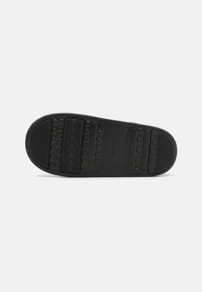 Semelle de chaussure en caoutchouc noir avec des motifs texturés, des grips circulaires et des rainures horizontales pour l'adhérence et la durabilité.