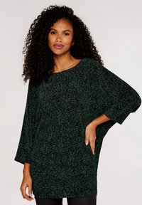 Grøn tunika i textured stof med bred halsudskæring, trekvart ærmer og løs pasform, prydet med et subtilt mønster gennem hele stoffet.