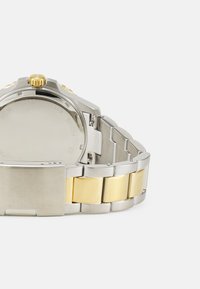 Montre en acier inoxydable argentée et dorée avec une lunette lisse, une couronne texturée et un bracelet en métal combiné comportant des maillons alternés.