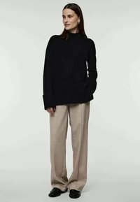 Mustarmust kõrge kaelusega sviiter on kombineeritud beežide laiade pükstega. Tekstuur näib olevat sile ning riietus on mugava lõikega. Jalatsiteks on mustad lamedad kingad.