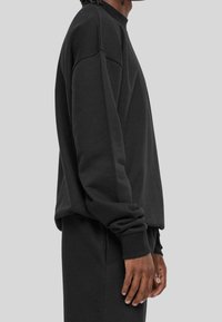 Svart sweatshirts i mjukt tyg, med avslappnad passform, hög krage och ribbad mudd. Texturen ser slät och enhetlig ut.