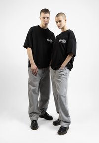 Black oversized t-shirts with a logo, paired with light gray baggy jeans and black boots, positioned against a white background.