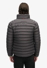 Grijze gevoerde jas met horizontale stiksels, hoge kraag en mer logo op de achterkant. Heeft een gestructureerde stof en ribbels aan de mouwen.